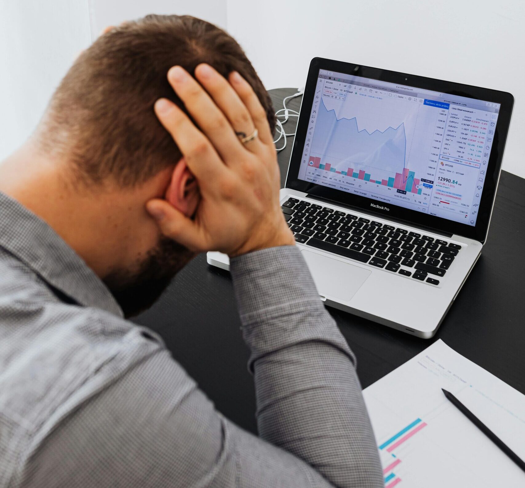 Businessman holding head in frustration, analyzing financial charts on laptop.