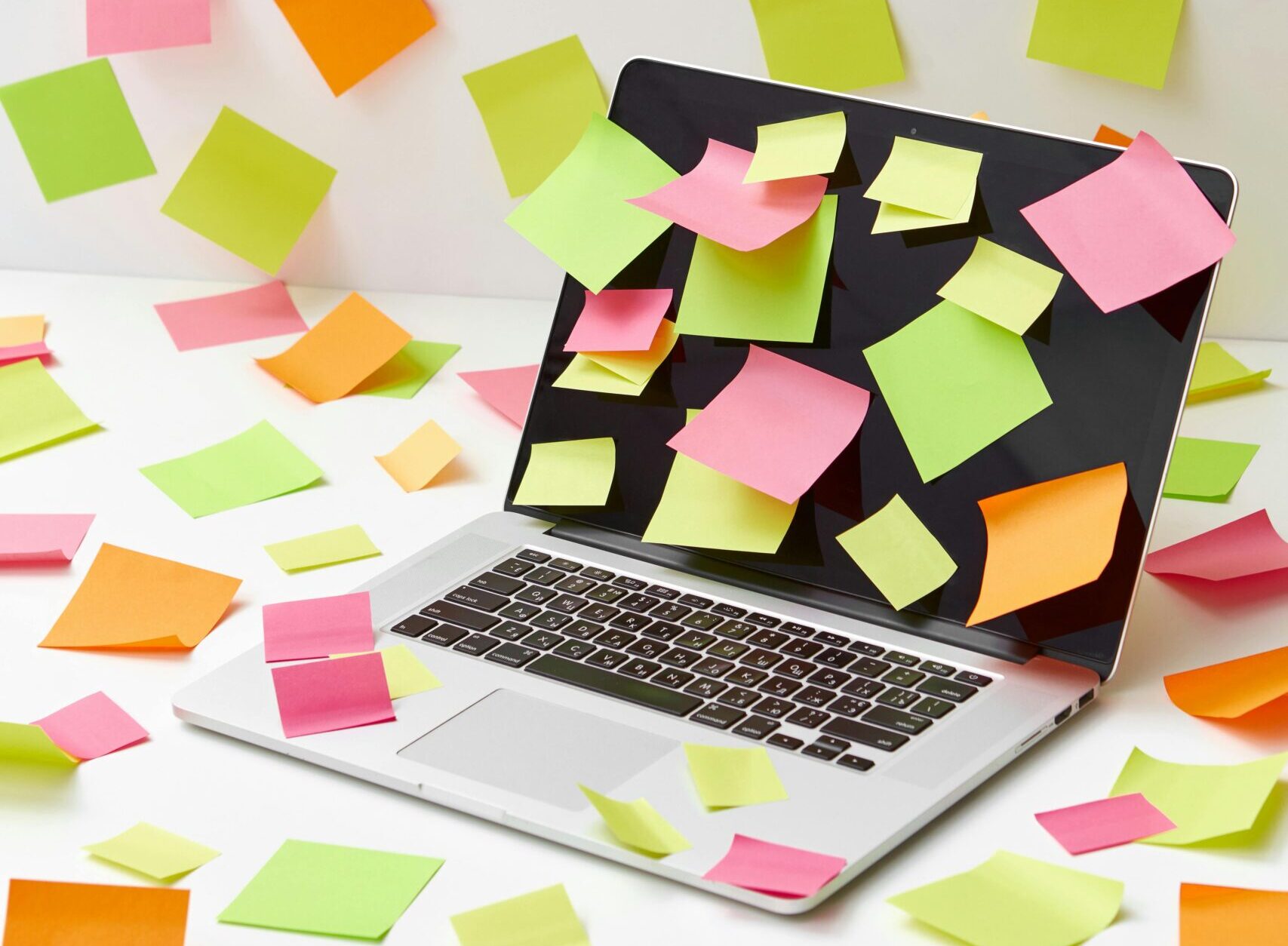 Laptop covered in sticky notes, with vibrant papers scattered around, captures creative chaos.